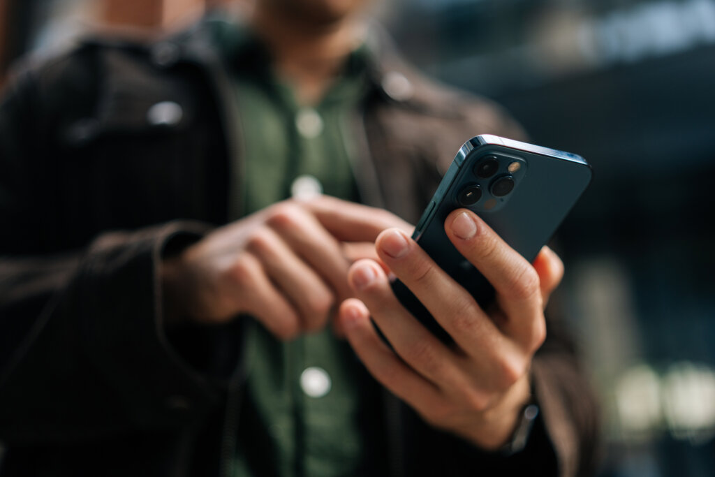 Close-up hands of unrecognizable man holding and using smartphone standing on city street, browsing internet, checking social media, using mobile application. Concept of modern communication.